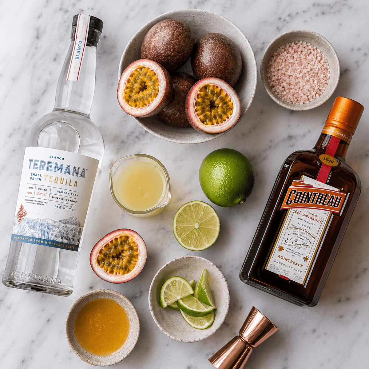 Overhead shot of lilikoi margarita ingredients including tequila, fresh passion fruit, limes, salt, and Cointreau
