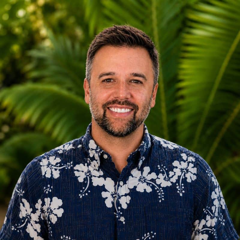 Bryan Murphy, host of Hawaii's Best Travel podcast, smiling in an aloha shirt with palm trees in the background
